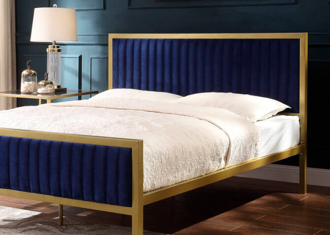 Royal blue velvet and golden steel frame bed with white bedding in a bedroom with dark grey accent wall